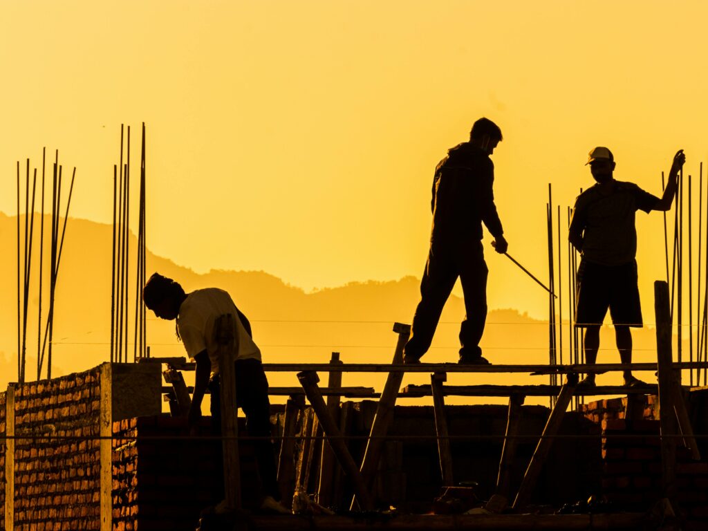 Silhouetted workers on a construction site at sunset, highlighting the manual labor involved.