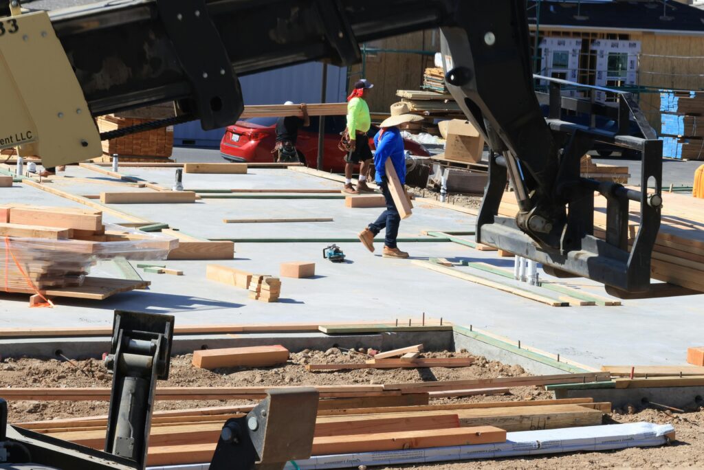 Construction workers actively building a structure with timber and machinery outdoors.