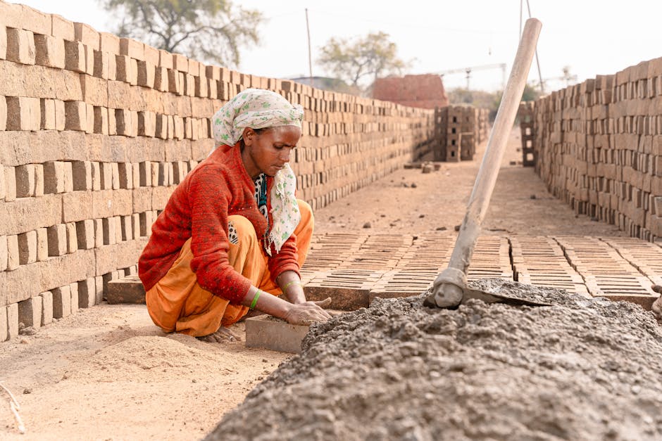 A woman is stacking bricks in a rural outdoor setting, showcasing traditional brick-making.