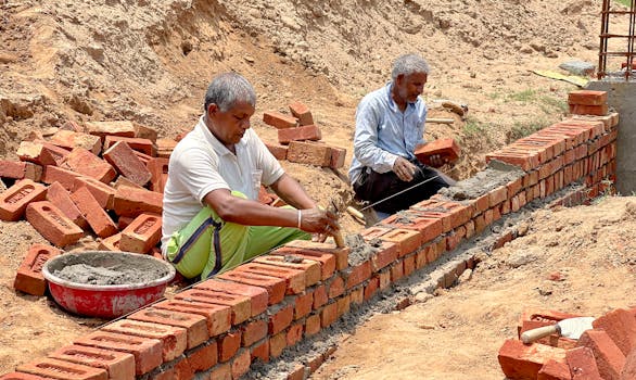 Two men laying bricks at a construction site in Rasulpur, India.